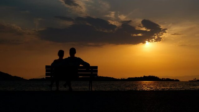 Family resting by colorful cloudscape. A man and woman silhouette resting together on the beach and watch the dusk in summer.