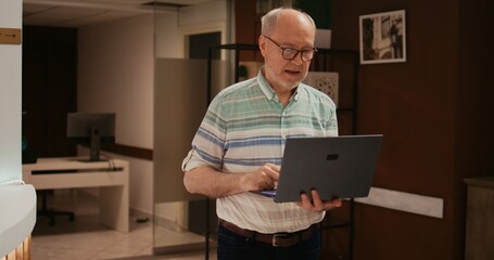 Older person searching for places to visit on laptop, using wireless connection at hotel before...