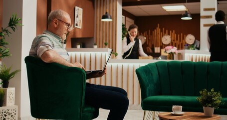 Elderly man searching for landmarks on laptop, using wireless network at five star hotel before registering process. Retired guest travelling on holiday, browsing online leisure activities.