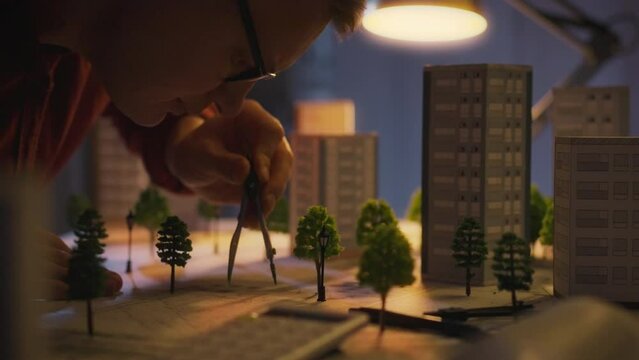 A white European male, equipped with tools, is engaged in the design and development of a residential area, engineering, working on landscape planning at night under the light of a table lamp