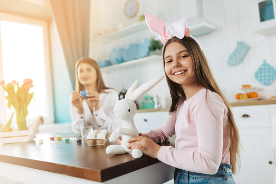 Attractive young woman with little cute girl and boy are preparing for Easter celebration. Happy family wearing bunny ears are spending time together before Easter while painting eggs