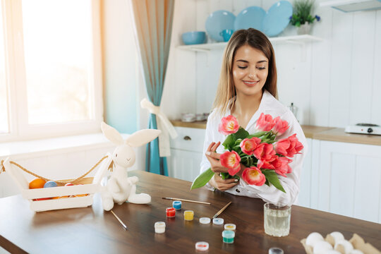 Happy Easter! Attractive woman holding bouquet of spring tulips and starting paint eggs for celebration