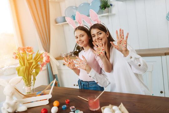 We are ready for Easter! Mom and daughter are having fun showing their hands on the camera stained with colorful Easter sweets, while they paint eggs preparing for the holiday