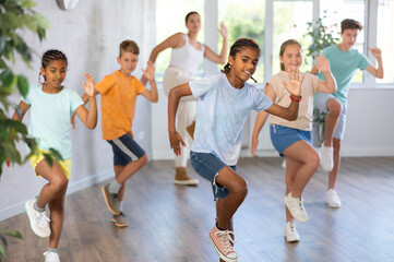 Active preteen children practicing Hip-hop dance with young teacher in training hall during dancing...