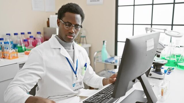 Focused african man in lab coat working with computer in a modern laboratory setting.