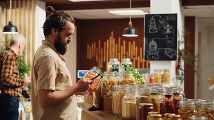 Zero waste supermarket customer shopping for pantry staples, using smartphone to take photo for wife at home. Man in local neighborhood shop using mobile phone to agree on what to buy with partner