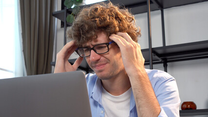 Tired unhappy young man wear eye glasses looking laptop headache depression worried problem  business online at home. Frightened businessman despair problems work loss job stress look at computer.