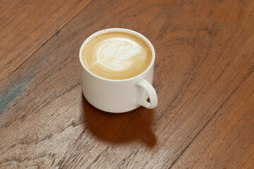 Mug cup of hot cappuccino art froth cream making flower on wooden table. Cup hot coffee fresh drawing pattern flower shaped milk froth foam on wood table. Beverage morning hot coffee art milk top v