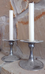 two white taper candlesticks in pewter holders against a stone wall