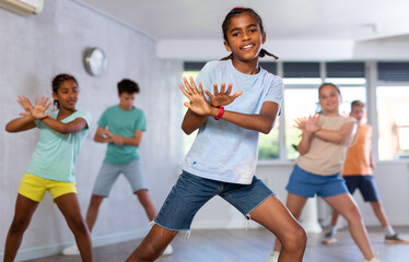 Positive juvenile boy engaged in Hip-hop dance together with children's group in training room...