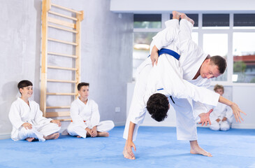 Experienced male karate instructor demonstrating attacking techniques in sparring with young...