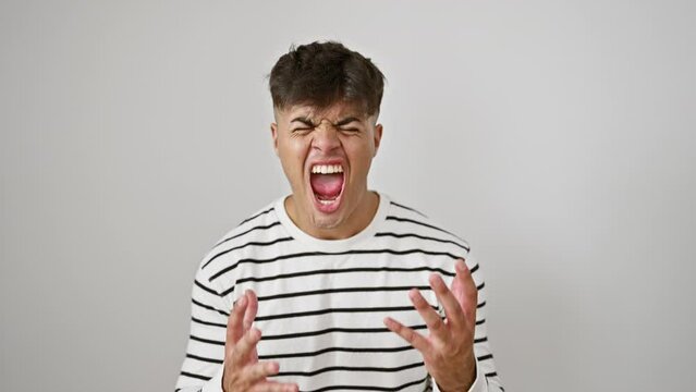 Frustrated young hispanic guy in stripes, crazy expression, mad shouting. arms raised in fury, stressed yell on isolated white background