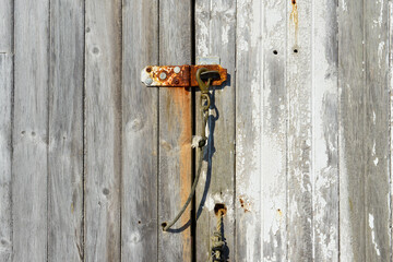 The exterior shed door of a vintage weathered building. The white paint is peeling from the worn...