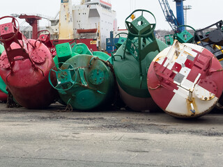 Red and green colored round spar buoys stacked in a marine supply yard. The markers float in the...