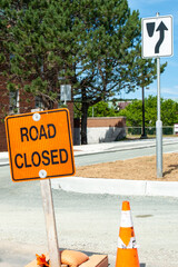 An orange colored road sign with a road closed in black lettering. The sign is in the foreground...