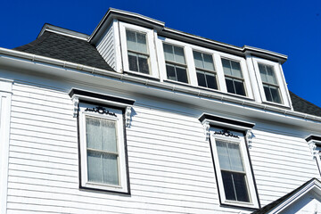A large vintage Mansard roof on a white wooden house. The attic has a shed dormer with five glass...