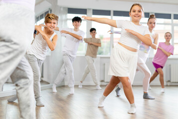 Female girl student repeats movements of unrecognizable teacher during group modern dance class. Hobbies, active pastime, additional extracurricular activities for children and teenagers