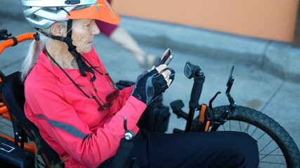 Elderly woman on recumbent e bike electric bicycle checking messages on phone, scrolling, looking...