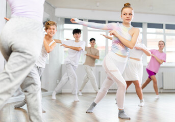 Team of positive teenagers rehearsing modern dances in dance hall