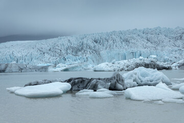 Heavy clouds over the icebergs floating in Fjallsarlon glacier lagoon lake in Iceland
