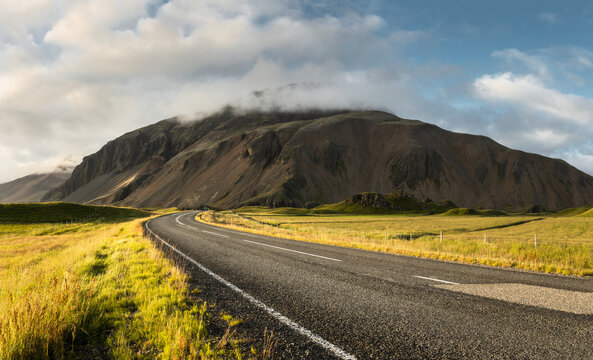 Winding road leading towards the mountain in southeast Iceland during sunny afternoon. Blue sky and clouds gathering over the hills.