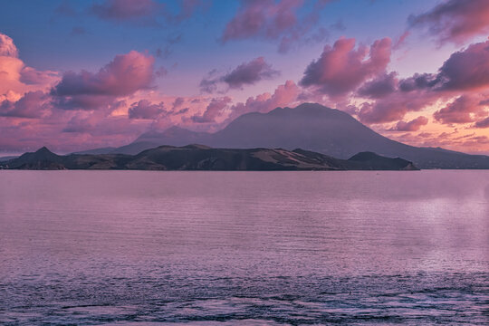 A serene scene of a mountain landscape by the sea, with pink and purple twilight skies reflecting on water