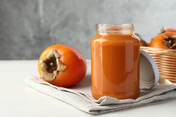 Delicious persimmon jam in glass jar and fresh fruits on white wooden table