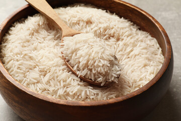 Raw basmati rice in bowl and spoon on table, closeup