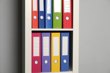 Colorful binder office folders on shelving unit near light grey wall