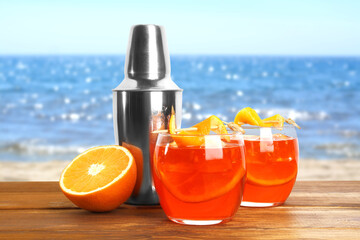Aperol spritz cocktail with orange slices in glasses and shaker on wooden table at beach