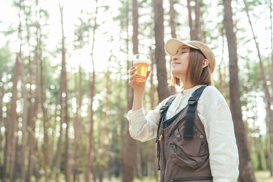キャンプ場でビールを飲む女性キャンパー（お酒・アルコール・クラフトビール・発泡酒）
