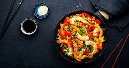 Hot stir fry shrimps with colorful paprika, green peas, chives and sesame seeds with ginger, garlic and soy sauce.   Black kitchen table background, top view - obrazy, fototapety, plakaty