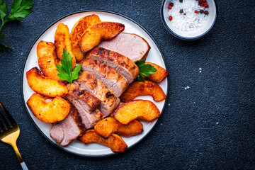 Baked pork tenderloin with spicy caramelized apples on plate, black table background, top view