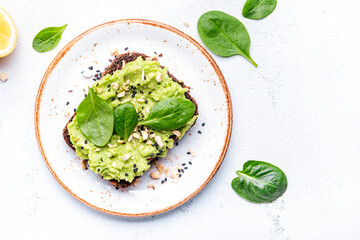 Obraz premium Avocado toasts with spinach and cashew nuts sprinkled with sesame seeds on white table background, top view