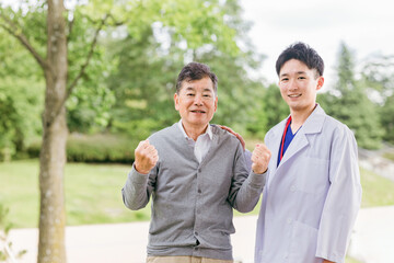 ガッツポーズをするシニア男性患者と若い男性医師（退院）
