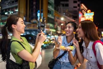 Asian women friend eating street food while traveling in city at night. 