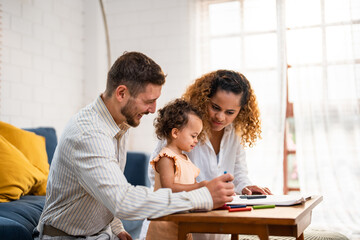 African American young daughter painting on paper with parents in house. 