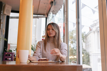 Woman with blonde hair sips cappuccino in a cafe. She is holding the glass up to her face, taking a...