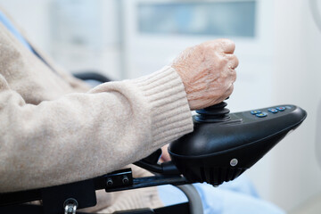 Asian elderly disability woman patient use joystick electric wheelchair in hospital.