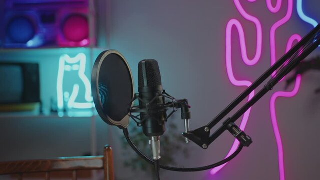 Professional condenser microphone with pop filter in modern recording studio with multicolored neon decor. Close-up shot, no people