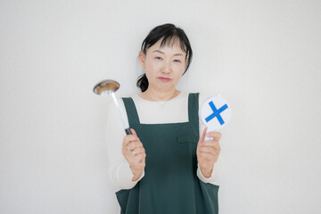 バツとおたまを持つ中高年女性