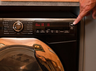close up view of a washing machine set to low temperature wash cyle to reduce cost and energy to clean laundry persons hand about to press start button