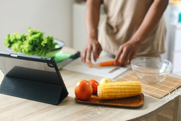 A tablet computer, corn and tomato on wooden tray with man making salad in the background