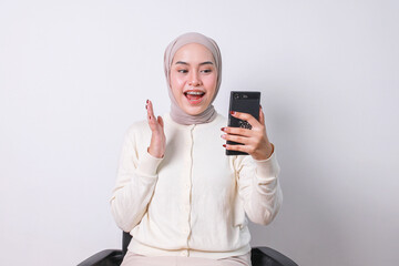 Young Asian moslem woman with braces making video call on smartphone while sitting on a chair