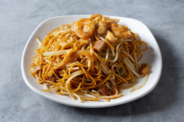 A view of a plate of chow mein, featuring shrimp, chicken and pork.