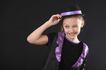 cheerful little girl wearing a black hat and vest in studio making funny facial expressions practicing acting skills