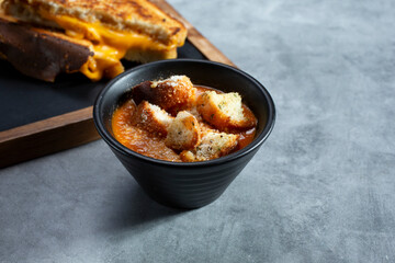 A view of a bowl of tomato basil soup, next to a grilled cheese sandwich.