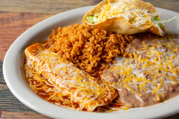 A view of a combo plate, featuring an enchilada, hard taco, rice and beans.