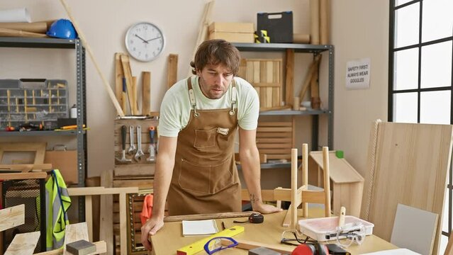Caucasian craftsman with beard wearing apron in carpentry workshop focused on woodworking