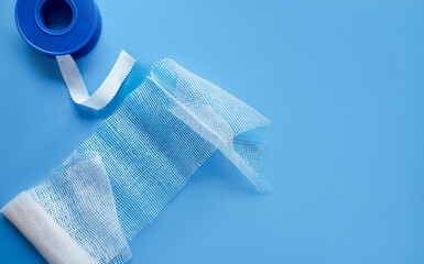 Blue medical bandage roll partially unraveled, with space for text on a solid blue background,...